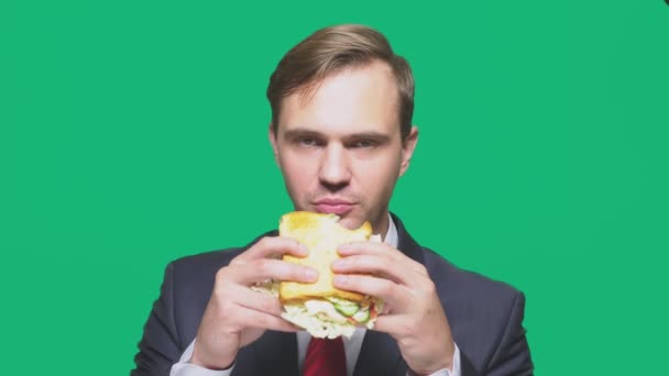 Hombre de negocios comiendo un sándwich sobre un fondo verde. concepto de almuerzo rápido — Vídeos de Stock