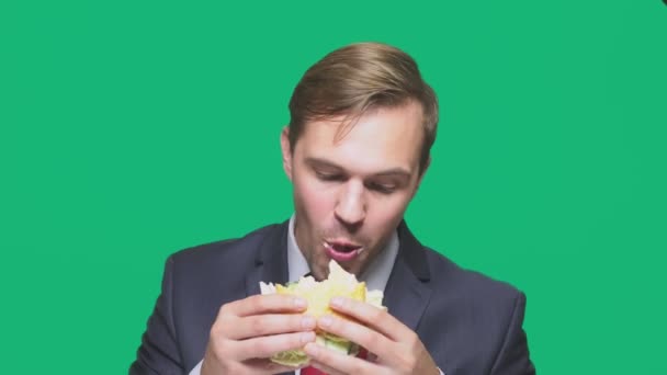 Empresário comendo uma sanduíche em um fundo verde. conceito de almoço rápido — Vídeo de Stock