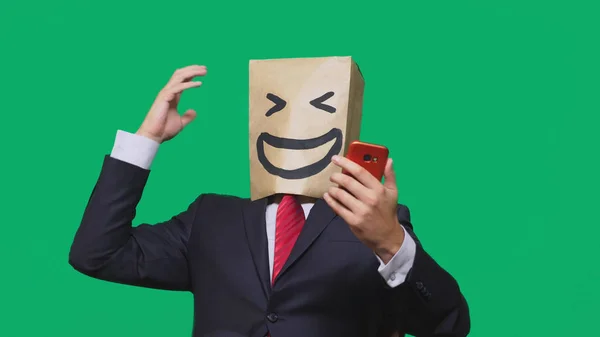 Conceito de emoções, gestos. um homem com sacos de papel na cabeça, com um emoticon pintado, sorriso, alegria. falando em um telefone celular — Fotografia de Stock