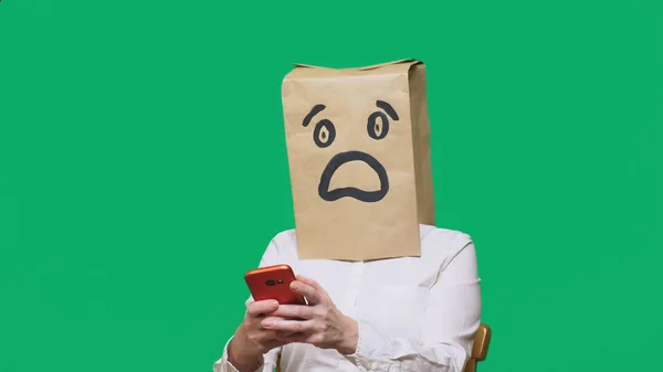 Concept van emoties, gebaren. een man met papieren zakken op zijn hoofd, met een geschilderde emoticon, vrees. praten op een mobiele telefoon — Stockfoto