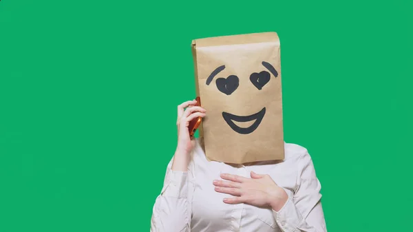 Conceito de emoções, gestos. um homem com sacos de papel na cabeça, com um emoticon pintado, sorriso, alegria, amor. falando em um telefone celular — Fotografia de Stock