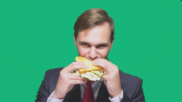 Geschäftsmann, der ein Sandwich auf grünem Hintergrund isst. Konzept für schnelles Mittagessen — Stockfoto