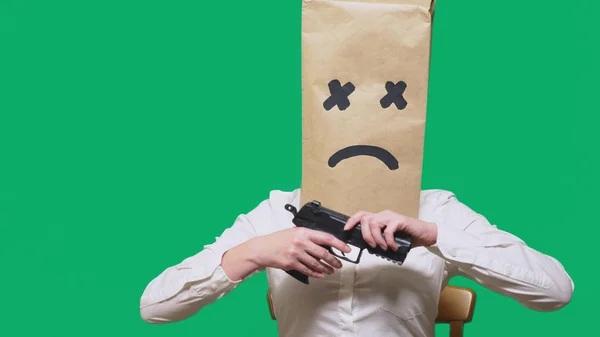 Концепция эмоций, жестов. a man with a package on his head, with a painted smiley, exhausted, tired, holding a gun . — стоковое фото