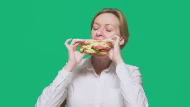 Iş kadını yeşil bir arka plan üzerinde bir sandviç yeme. Hızlı öğle yemeği kavramı. — Stok video