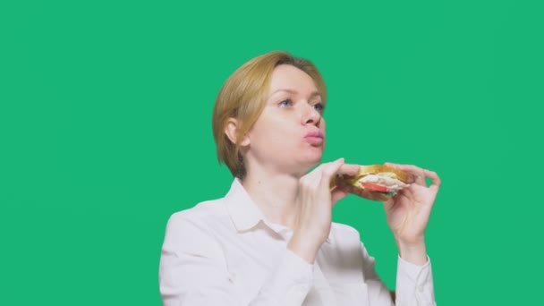 Iş kadını yeşil bir arka plan üzerinde bir sandviç yeme. Hızlı öğle yemeği kavramı. — Stok video