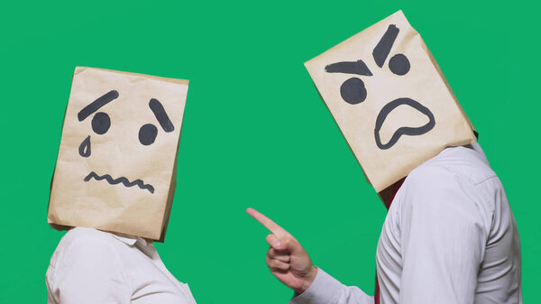 The concept of emotions and gestures. Two people in paper bags with smileys. Aggressive smiley swears. The second crying sad