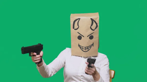 Concept van emotie, gebaren. een man met een pakket op zijn hoofd, met een geschilderde smiley boos, sluwe, leedvermaak, duivel, pistolen in handen — Stockfoto