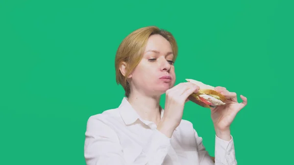 Mulher de negócios comendo uma sanduíche em um fundo verde. conceito de almoço rápido . — Fotografia de Stock