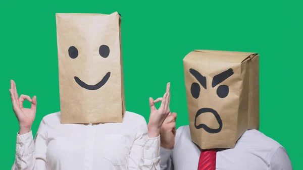 Das Konzept der Emotionen und Gesten. zwei Personen in Papiertüten auf dem Kopf mit aufgemalten Smileys. Aggressiver Smiley flucht. der zweite lächelt ihn an. — Stockfoto