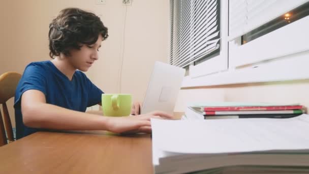 Jongen tiener gegoten thee op de laptop. huiswerk, online learning, 4 k close-ups, — Stockvideo