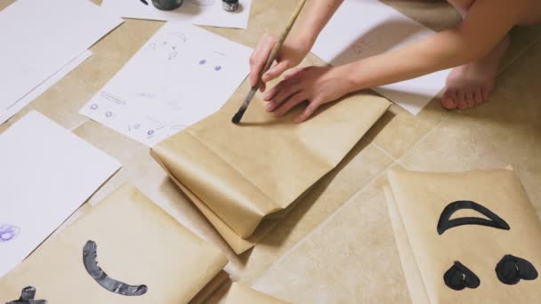 La fille dessine avec un pinceau sur des sacs en papier diverses émotions. Le concept des émotions dans les sourires — Video