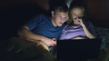 Çift, erkek ve kadın, bir dizüstü bilgisayarda bir yatak yatak odası yatmadan önce bir film izlerken. heyecan verici bir film seyrederken, seyirci ilgi ile çeşitli duyguların yaşandığı izliyor.