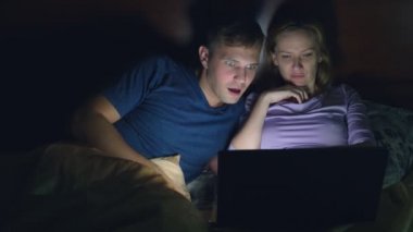 Çift, erkek ve kadın, bir dizüstü bilgisayarda bir yatak yatak odası yatmadan önce bir film izlerken. heyecan verici bir film seyrederken, seyirci ilgi ile çeşitli duyguların yaşandığı izliyor.