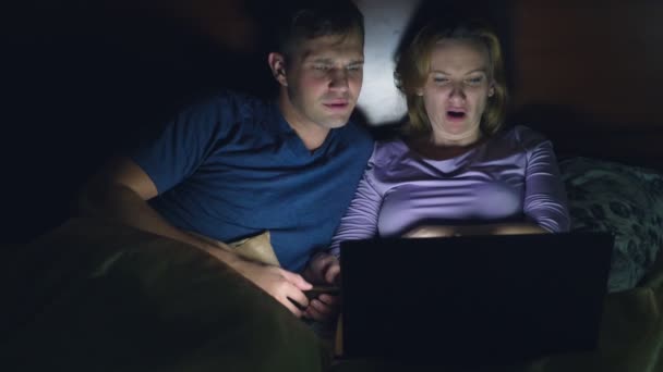 Couple, homme et femme, regardant un film sur un ordinateur portable sur un lit dans la chambre avant de se coucher. regarder un film d'horreur, les téléspectateurs ont peur et dégoûté — Video