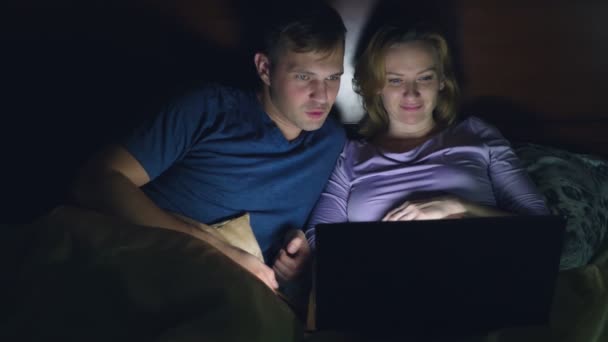 Пара, чоловік і жінка, дивиться фільм на ноутбуці на ліжку в спальні перед сном. перегляд захоплюючого фільму, аудиторія з цікавістю дивиться, відчуває різні емоції . — стокове відео