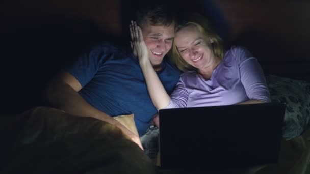 Couple, homme et femme, regardant un film sur un ordinateur portable sur un lit dans la chambre avant de se coucher. regarder un film comique, le public rit . — Video