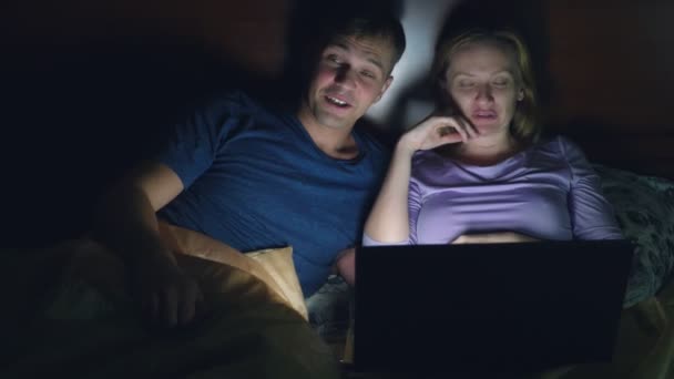 Couple, man and woman, watching a movie on a laptop on a bed in the bedroom before bed. watching an exciting movie, the audience is watching with interest, experiencing various emotions. — Stock Video