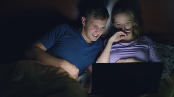 Pareja, hombre y mujer, viendo una película en un portátil en una cama en el dormitorio antes de acostarse. viendo una película emocionante, el público está viendo con interés, experimentando varias emociones . — Vídeos de Stock