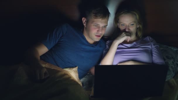 Pár, muž a žena, sledovat film v přenosném počítači na posteli v ložnici před spaním. sledovat vzrušující film, publikum sleduje se zájmem, zažívá různé emoce. — Stock video