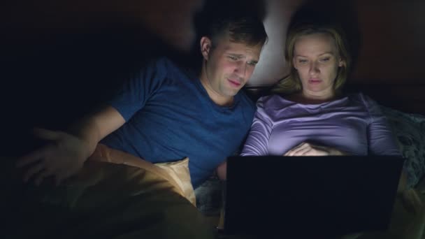 Coppia, uomo e donna, guardando un film su un computer portatile su un letto in camera da letto prima di andare a letto. guardando un film emozionante, il pubblico sta guardando con interesse, vivendo varie emozioni . — Video Stock