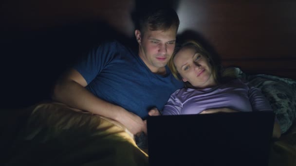 Casal, homem e mulher, assistindo a um filme em um laptop em uma cama no quarto antes de dormir. assistir a um filme chato, adormecer enquanto assiste a um filme — Vídeo de Stock