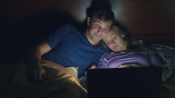 Casal, homem e mulher, assistindo a um filme em um laptop em uma cama no quarto antes de dormir. assistir a um filme chato, adormecer enquanto assiste a um filme — Vídeo de Stock