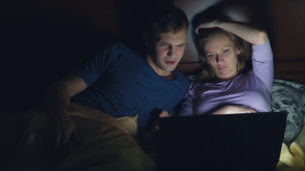 Casal, homem e mulher, assistindo a um filme em um laptop em uma cama no quarto antes de dormir. assistir a um filme chato, adormecer enquanto assiste a um filme — Vídeo de Stock