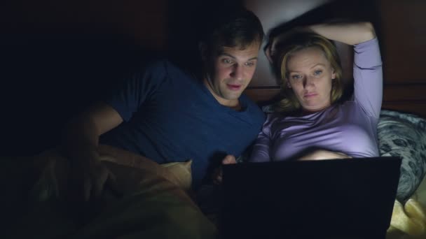 Casal, homem e mulher, assistindo a um filme em um laptop em uma cama no quarto antes de dormir. assistir a um filme chato, adormecer enquanto assiste a um filme — Vídeo de Stock