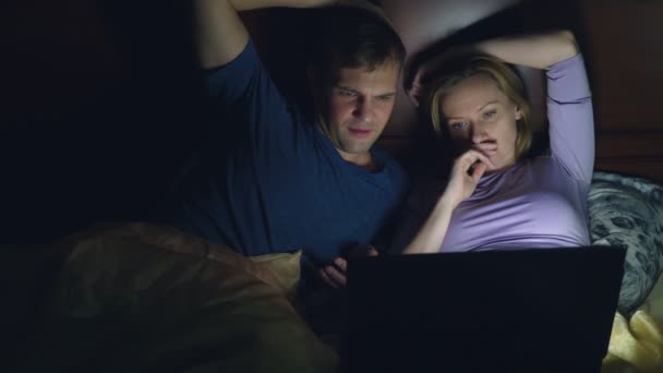 Pár, a férfi és a nő, egy film, egy laptop, egy ágyon a hálószobában, lefekvés előtt. egy unalmas film, a film nézése közben elalszik — Stock videók