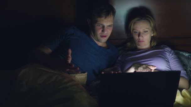 Paar, man en vrouw, lettend op een film op een laptop op een bed in de slaapkamer voor het slapen. kijken naar een spannende film, is het publiek kijken met belangstelling, verschillende emoties ervaren. — Stockvideo