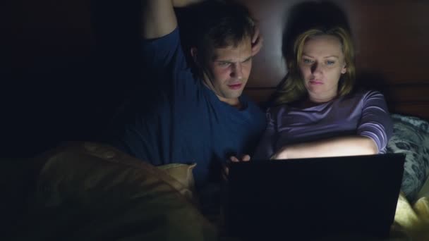 Pár, muž a žena, sledovat film v přenosném počítači na posteli v ložnici před spaním. sledovat vzrušující film, publikum sleduje se zájmem, zažívá různé emoce. — Stock video