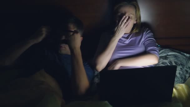 Couple, homme et femme, regardant un film sur un ordinateur portable sur un lit dans la chambre avant de se coucher. regarder un film ennuyeux, s'endormir en regardant un film — Video