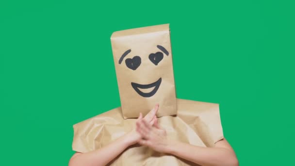 感情、ジェスチャーの概念。塗られた顔、笑顔、喜びと彼の頭に紙袋を持つ男の目が大好き. — ストック動画
