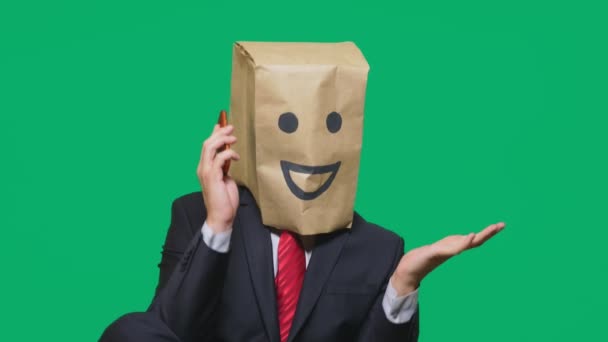 Concepto de emociones, gestos. un hombre con bolsas de papel en la cabeza, con un emoticono pintado, sonrisa, alegría. hablando por un teléfono celular — Vídeos de Stock