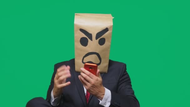 Konzept der Emotion, Gesten. ein Mann mit einem Paket auf dem Kopf, mit einem aufgemalten Smiley aggressiv, wütend. Telefonieren auf dem Handy — Stockvideo
