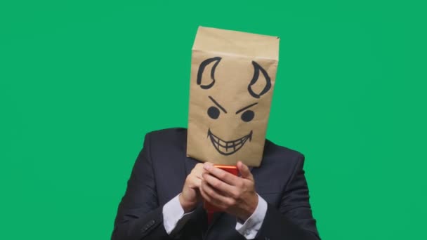 Concept of emotions, gestures. a man with a package on his head, with a painted black smiley face, a devil, crafty, gloating, talking on a mobile phone. — Stock Video