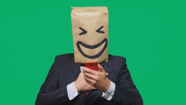 Concepto de emociones, gestos. un hombre con bolsas de papel en la cabeza, con un emoticono pintado, sonrisa, alegría. hablando por un teléfono celular — Vídeo de stock