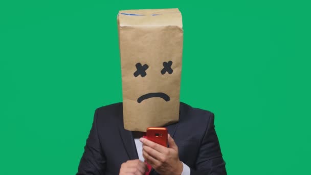 Concept van emotie, gebaren. een man met een pakket op zijn hoofd, met een geschilderde smiley, uitgeput, moe, praten over de telefoon — Stockvideo