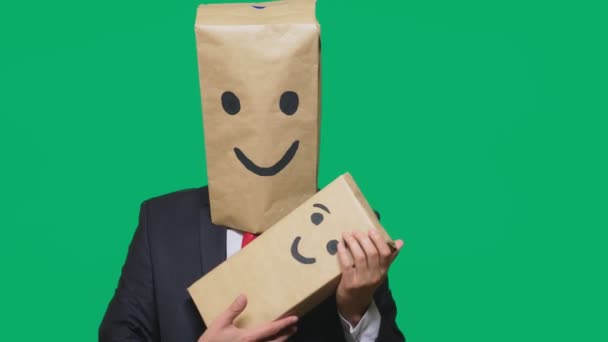 Konzept der Emotionen, Gesten. Mann mit einem Paket auf dem Kopf, mit einem aufgemalten Emoticon, Lächeln, Freude, Lachen. spielt mit dem Kind, das auf die Schachtel gemalt ist. — Stockvideo