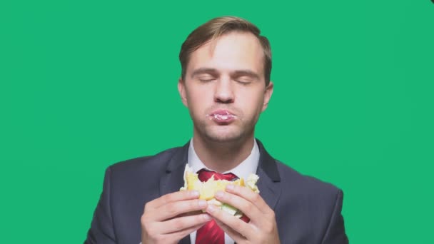 Επιχειρηματίας που τρώει ένα σάντουιτς σε πράσινο φόντο. γρήγορο γεύμα έννοια — Αρχείο Βίντεο