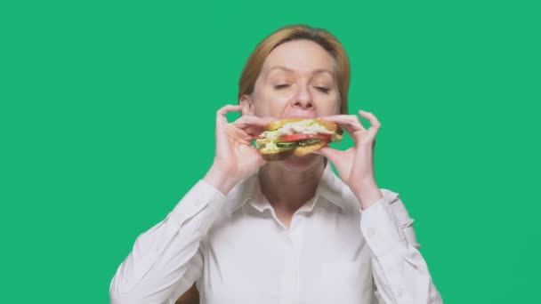 Zakenvrouw eten van een boterham op een groene achtergrond. snelle lunch concept. — Stockvideo