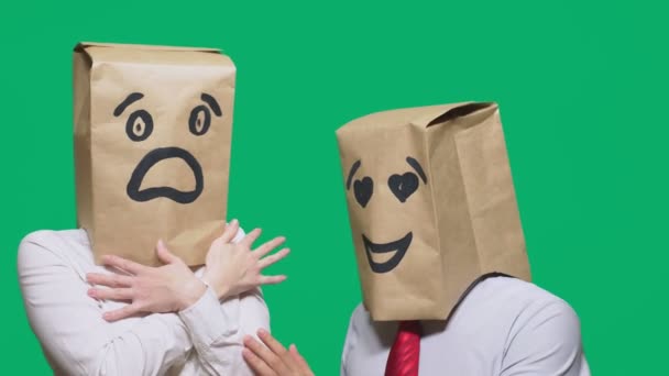 Konzept der Emotionen, Gesten. Ein paar Menschen mit Tüten auf dem Kopf, mit einem aufgemalten Emoticon, einem Lächeln, verliebten Augen und dem zweiten mit einer Maske des Schreckens, der Angst. Konzept der sexuellen Belästigung — Stockvideo