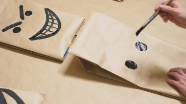 Kız bir fırça ile çeşitli duygular kağıt torbaları üzerinde çizer. Suratlar duygular kavramı