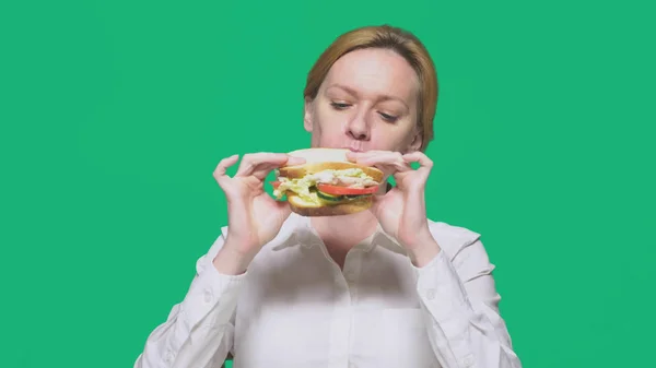 Mulher de negócios comendo uma sanduíche em um fundo verde. conceito de almoço rápido . — Fotografia de Stock