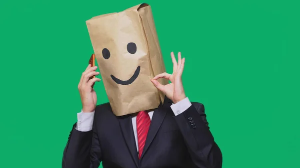 Concepto de emociones, gestos. un hombre con bolsas de papel en la cabeza, con un emoticono pintado, sonrisa, alegría. hablando por un teléfono celular — Foto de Stock