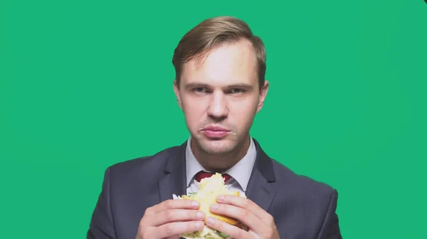 Empresário comendo uma sanduíche em um fundo verde. conceito de almoço rápido — Fotografia de Stock