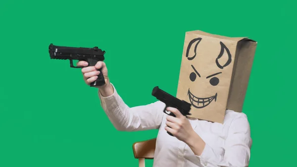 Konzept der Emotion, Gesten. ein Mann mit einem Paket auf dem Kopf, mit einem aufgemalten Smiley wütend, listig, schwärmerisch, Teufel, Pistolen in der Hand — Stockfoto