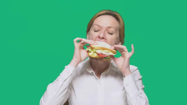 Mujer de negocios comiendo un sándwich sobre un fondo verde. concepto de almuerzo rápido . — Foto de Stock