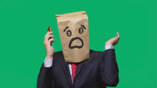 Concept of emotions, gestures. a man with paper bags on his head, with a painted emoticon, fear. talking on a cell phone — Stock Photo, Image