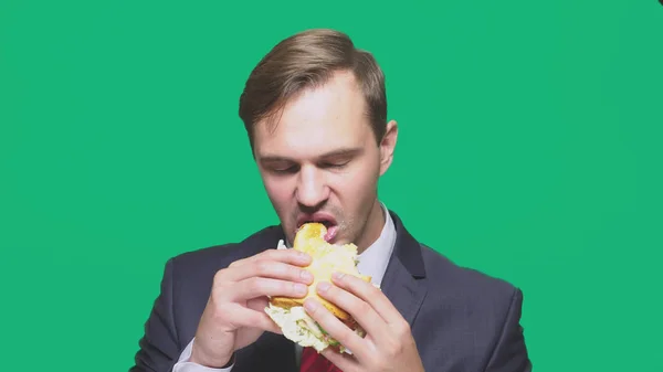 Empresário comendo uma sanduíche em um fundo verde. conceito de almoço rápido — Fotografia de Stock